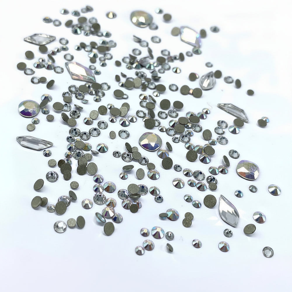 A collection of Swarovski 2058 XILION round and special shaped flatback crystals for nail art, clear with colorless AB coating, scattered on a white surface.