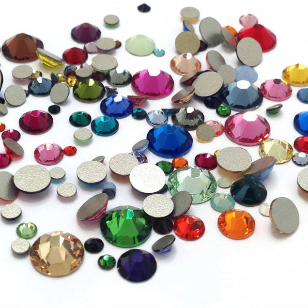 A pile of colorful flat-back rhinestones and adhesive gems on a plain white background, showing a variety of colors and sizes.